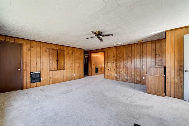 carpeted spare room with ceiling fan, heating unit, and wood walls