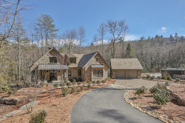 view of front of house featuring aphalt driveway, an outbuilding, stone siding, and a standing seam roof