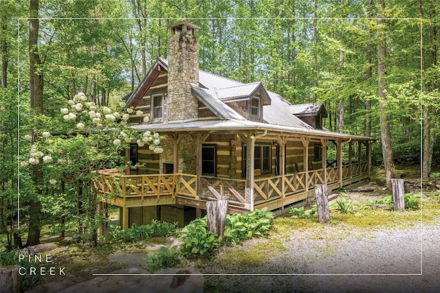 view of side of home with covered porch, log siding, a chimney, metal roof, and a forest view