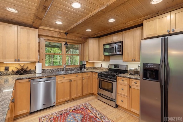 kitchen with appliances with stainless steel finishes, decorative light fixtures, beamed ceiling, sink, and dark stone counters