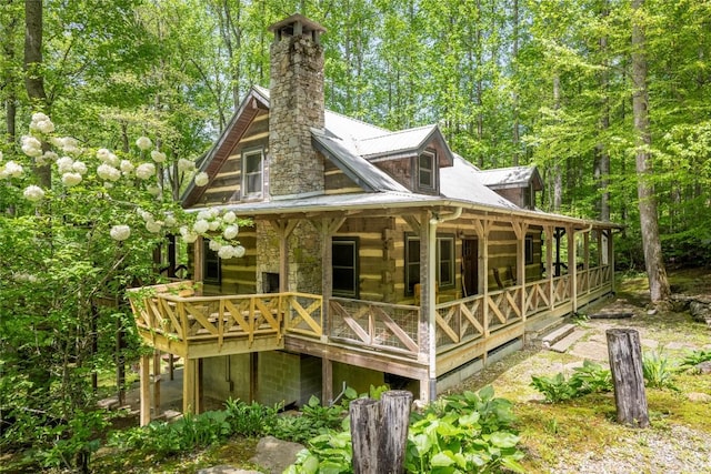 rear view of property featuring covered porch, a chimney, metal roof, and log exterior