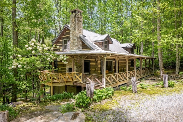 view of home's exterior with log exterior, a porch, a chimney, and metal roof