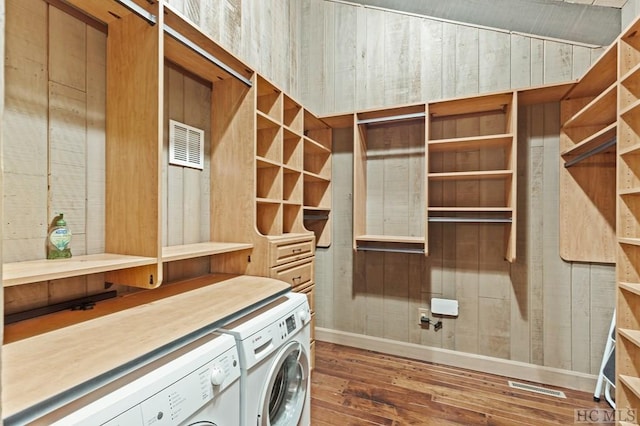 laundry area featuring separate washer and dryer, dark hardwood / wood-style flooring, and wood walls