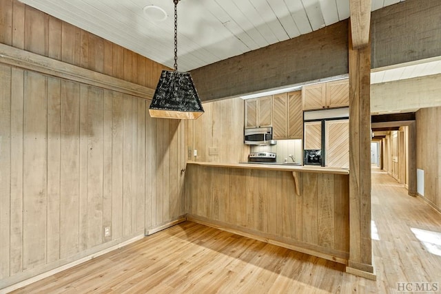 kitchen with wood walls, light brown cabinets, appliances with stainless steel finishes, kitchen peninsula, and pendant lighting