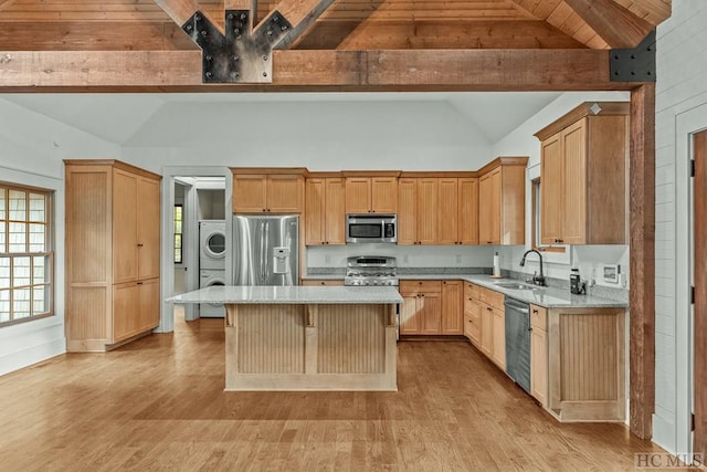 kitchen featuring appliances with stainless steel finishes, sink, stacked washer and clothes dryer, a center island, and light stone counters