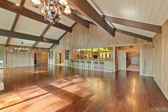 unfurnished living room with a notable chandelier, beam ceiling, hardwood / wood-style floors, and wood walls