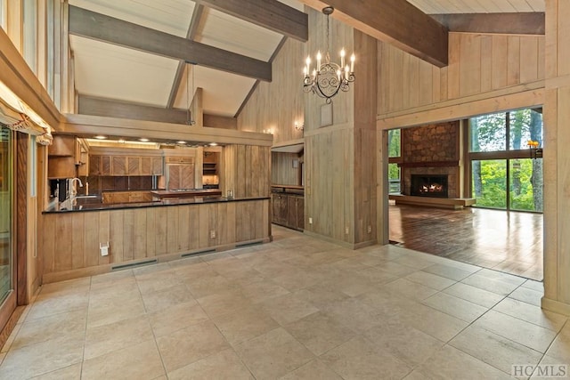 kitchen featuring light tile patterned floors, hanging light fixtures, wooden walls, high vaulted ceiling, and a fireplace