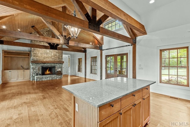 kitchen with light stone counters, light hardwood / wood-style floors, a kitchen island, french doors, and beamed ceiling