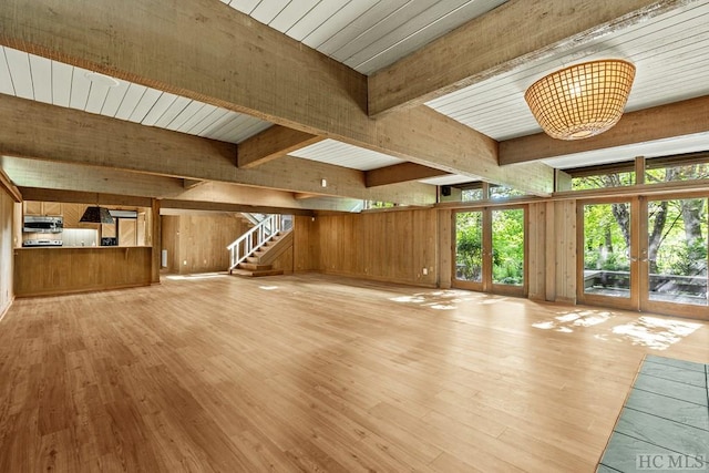 unfurnished living room featuring light hardwood / wood-style flooring, wood walls, and french doors