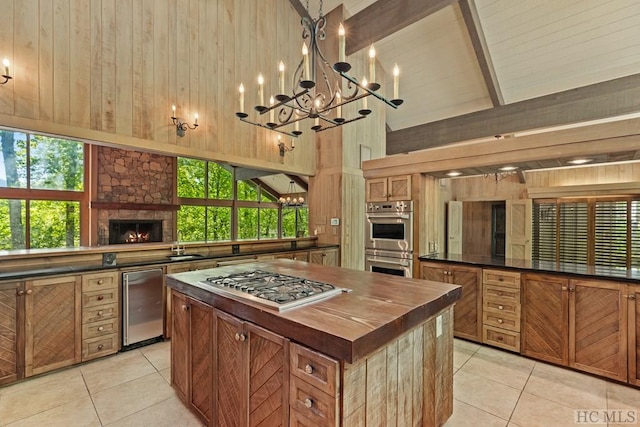 kitchen featuring light tile patterned flooring, appliances with stainless steel finishes, high vaulted ceiling, and wood walls