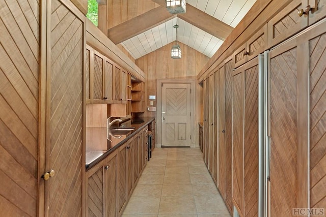 interior space with light tile patterned flooring, pendant lighting, wooden walls, lofted ceiling, and sink