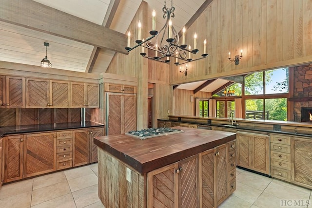 kitchen with hanging light fixtures, light tile patterned flooring, beamed ceiling, and wood walls