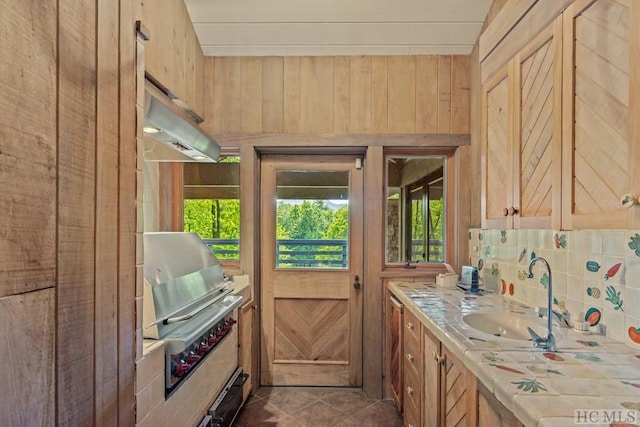 kitchen featuring light brown cabinetry, sink, wood walls, tile counters, and dark tile patterned floors