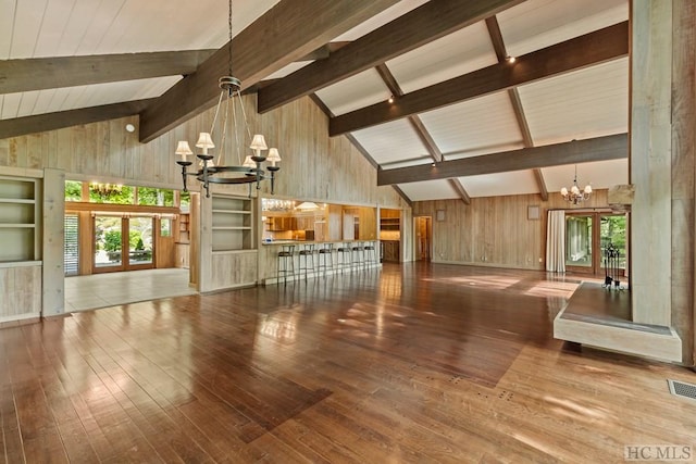 unfurnished living room with french doors, wooden walls, a notable chandelier, hardwood / wood-style flooring, and beam ceiling