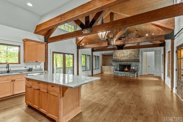 kitchen with sink, a center island, light stone counters, beamed ceiling, and light wood-type flooring