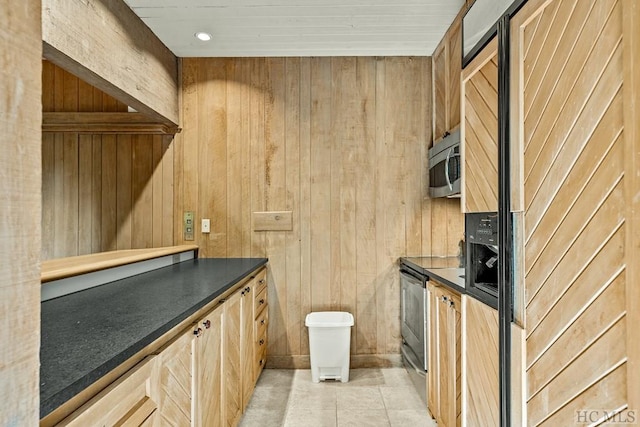 kitchen featuring light tile patterned floors, light brown cabinets, stainless steel appliances, and wood walls