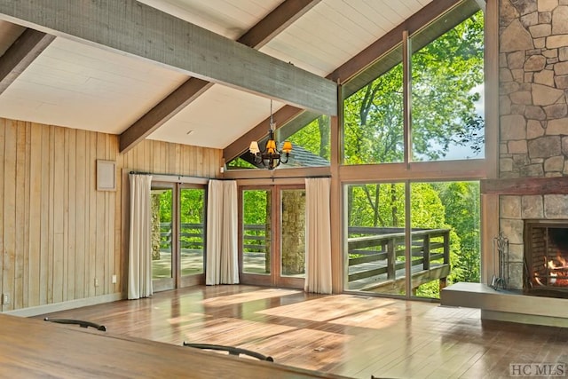 unfurnished sunroom with a stone fireplace, vaulted ceiling with beams, and a chandelier