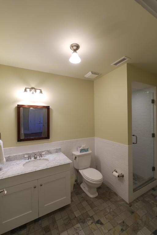 bathroom featuring toilet, a wainscoted wall, vanity, tile walls, and a shower stall