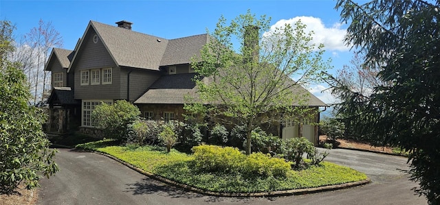exterior space featuring roof with shingles, a chimney, and aphalt driveway