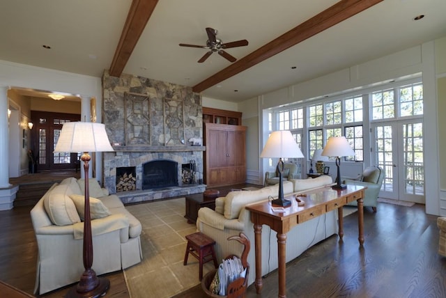 living area featuring a stone fireplace, a ceiling fan, french doors, beam ceiling, and ornate columns