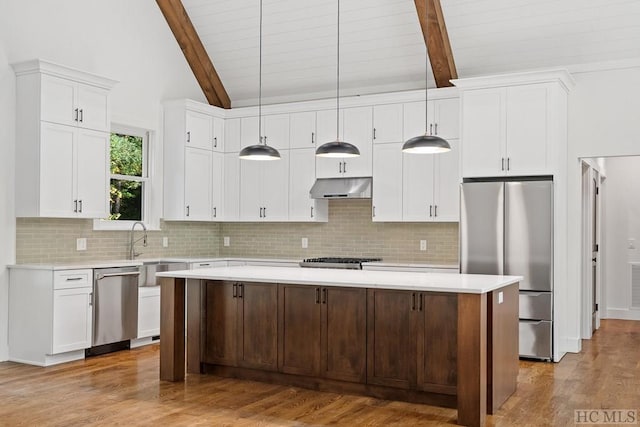 kitchen with appliances with stainless steel finishes, beam ceiling, a center island, light hardwood / wood-style floors, and decorative light fixtures