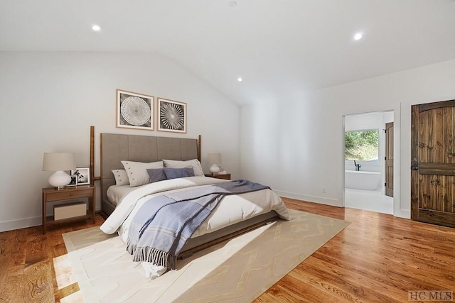 bedroom featuring light hardwood / wood-style floors, vaulted ceiling, and connected bathroom