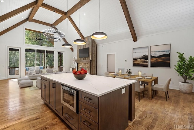 kitchen with hanging light fixtures, high vaulted ceiling, stainless steel microwave, beamed ceiling, and light wood-type flooring