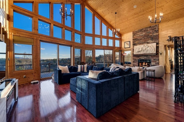 living room featuring dark hardwood / wood-style flooring, high vaulted ceiling, a stone fireplace, and an inviting chandelier