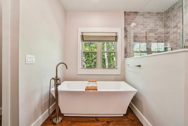 full bathroom with baseboards, a freestanding tub, wood finished floors, and tiled shower