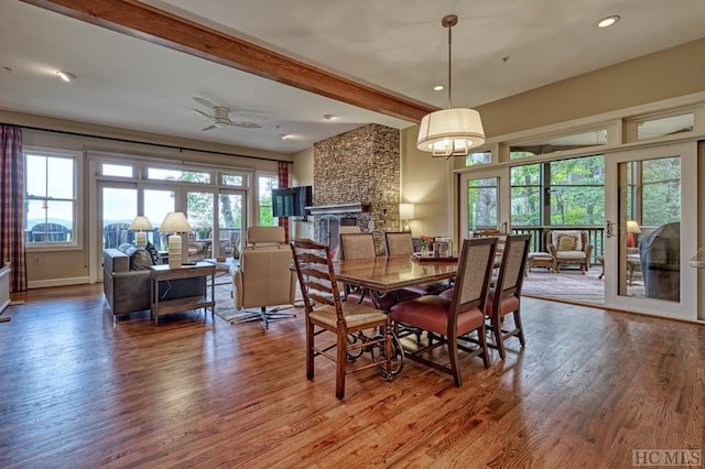 dining space with beamed ceiling, a large fireplace, wood-type flooring, and ceiling fan