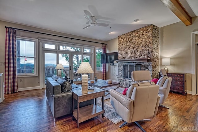 living room with a stone fireplace, hardwood / wood-style floors, ceiling fan, beam ceiling, and french doors