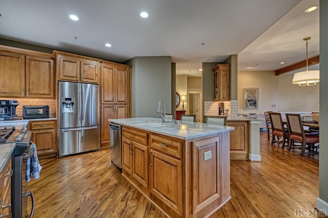 kitchen with appliances with stainless steel finishes, decorative light fixtures, tasteful backsplash, light stone counters, and a center island with sink