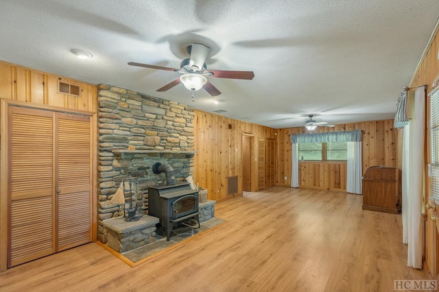 unfurnished living room featuring light wood-style floors, a wood stove, wood walls, and a textured ceiling