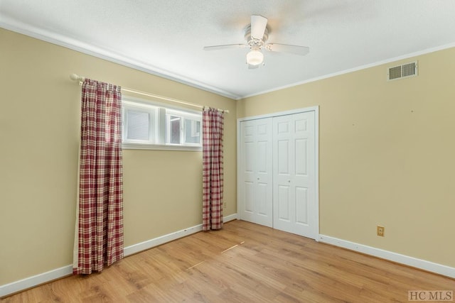 unfurnished bedroom featuring visible vents, baseboards, light wood-style floors, ornamental molding, and a closet