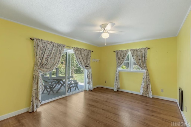 spare room featuring a textured ceiling, wood finished floors, a ceiling fan, baseboards, and ornamental molding