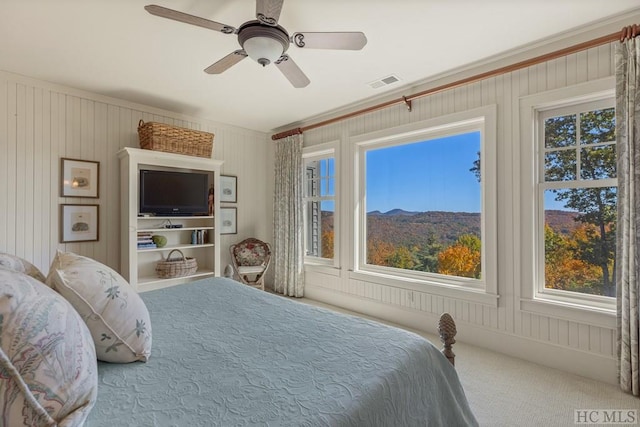 bedroom with ornamental molding, carpet floors, wooden walls, and ceiling fan