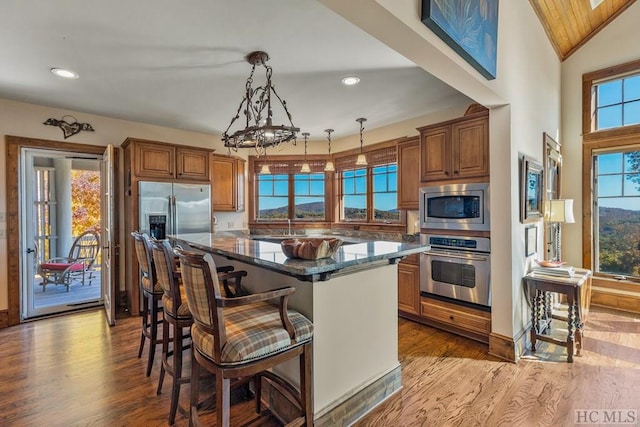 kitchen with a breakfast bar, a center island, appliances with stainless steel finishes, pendant lighting, and dark stone counters