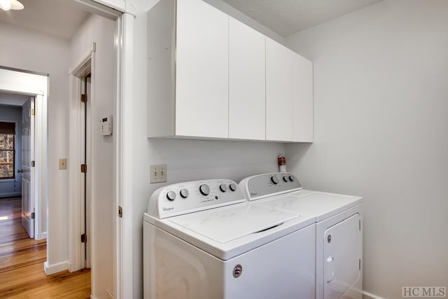 washroom featuring washing machine and dryer, cabinets, and light hardwood / wood-style flooring