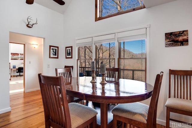 dining area with light wood-type flooring, a high ceiling, and ceiling fan