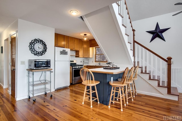 kitchen featuring light wood-type flooring, kitchen peninsula, stainless steel appliances, sink, and a kitchen breakfast bar