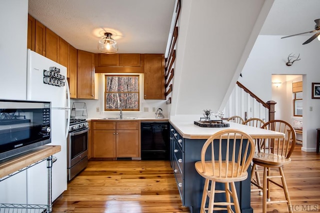 kitchen featuring appliances with stainless steel finishes, ceiling fan, a breakfast bar, sink, and light wood-type flooring