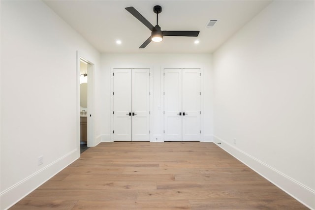 unfurnished bedroom featuring light wood finished floors, baseboards, visible vents, and multiple closets