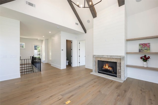 unfurnished living room with a warm lit fireplace, wood finished floors, an inviting chandelier, and visible vents