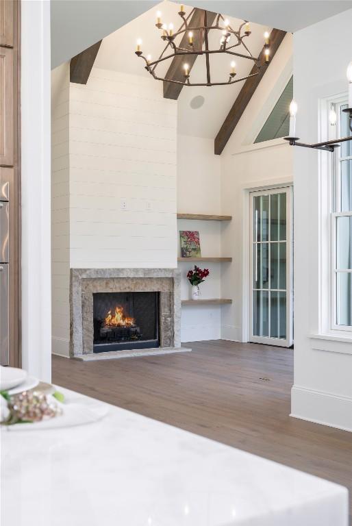 unfurnished living room featuring a lit fireplace, wood finished floors, vaulted ceiling with beams, a notable chandelier, and baseboards