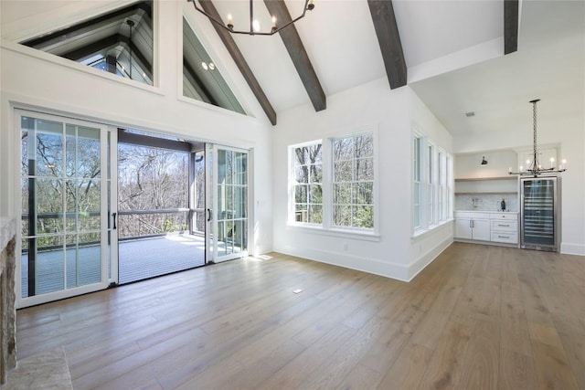 unfurnished living room featuring light wood-style floors, an inviting chandelier, beverage cooler, and beam ceiling