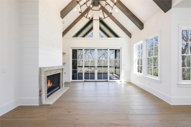 unfurnished living room with baseboards, beam ceiling, high vaulted ceiling, a high end fireplace, and wood finished floors