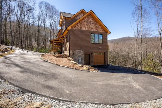 1086 Roaming Rd, Glenville, NC 28736 - view of side of home with driveway, an attached garage, stone siding, and a forest view