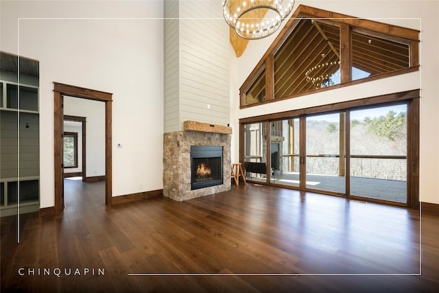 unfurnished living room with baseboards, a chandelier, a stone fireplace, a towering ceiling, and wood finished floors