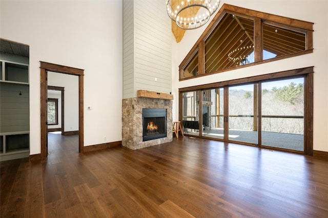 1086 Roaming Rd, Glenville, NC 28736 - unfurnished living room with baseboards, a towering ceiling, wood finished floors, a stone fireplace, and a notable chandelier