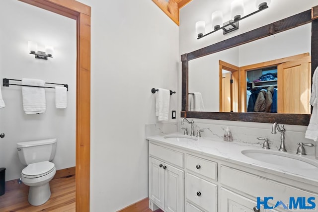 bathroom featuring double vanity, wood finished floors, a sink, and toilet